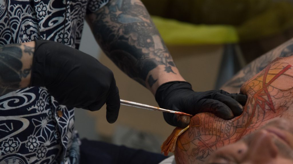 Dettaglio delle mani di un tatuatore che lavora con lo strumento tradizionale del tebori  