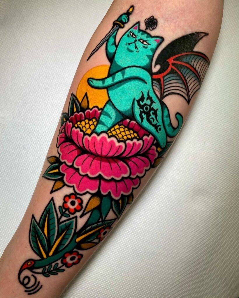 Artista: Marco Branchia. Pro Team Artist Water Law Tattoo. Tatuaggio a colori brillanti di un gatto color verde acqua con ali di pipistrello e un pugnale in mano, che si trova in equilibrio su una sola gamba su un fiore rosso magenta.